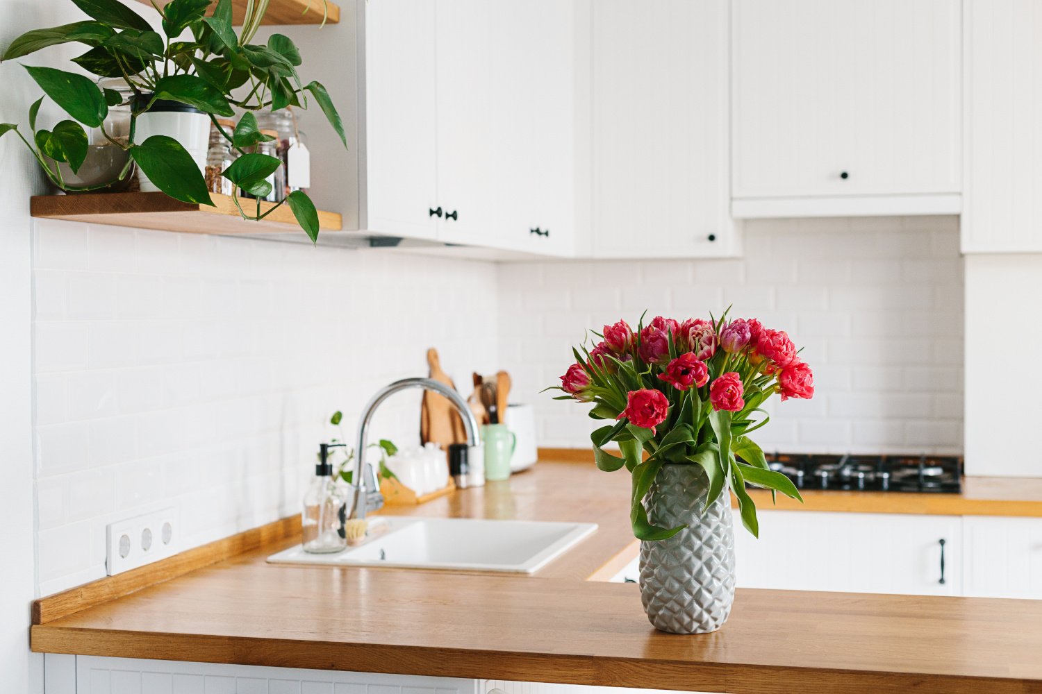 Modern all-white U-shaped kitchen with wood countertops and tulips placed on top in a vase